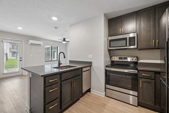 Modern apartment kitchen with dark cabinetry, stainless steel appliances, a center island with storage, and an open layout connected to the living area.