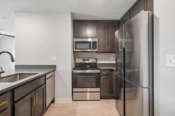 Apartment kitchen with dark cabinetry, stainless steel refrigerator, microwave, and oven, plus durable countertops and a functional galley-style layout.