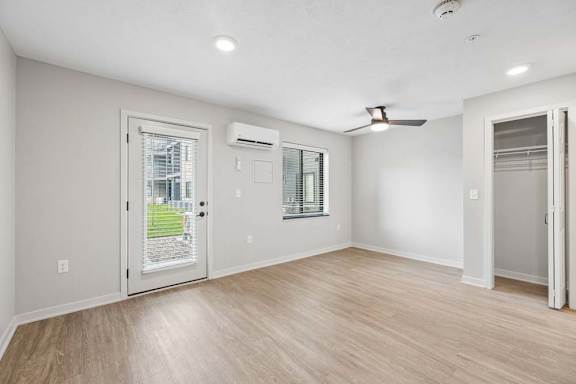 Bright apartment living room with wood-style flooring, recessed lighting, a glass patio door, ceiling fan, and an open closet near the entry.