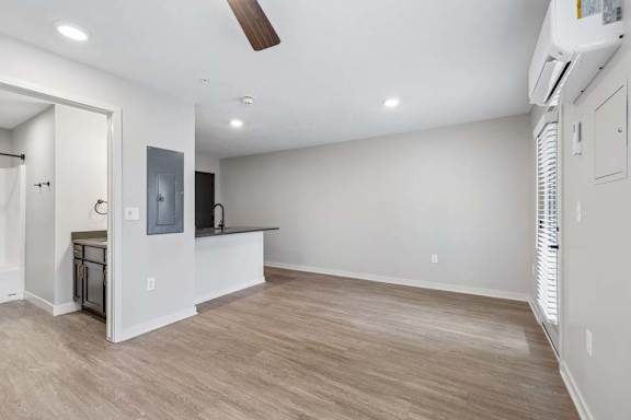 Spacious apartment living room with wood-style flooring, recessed lighting, a ceiling fan, and an open layout connecting to the kitchen with a breakfast bar.