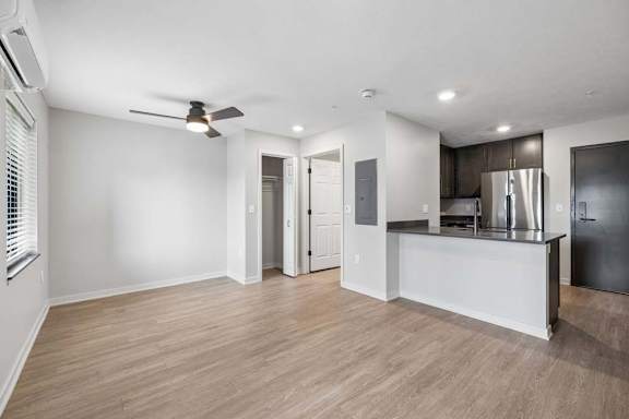 Open-concept apartment living area with wood-style flooring, a ceiling fan, and a kitchen featuring dark cabinetry, stainless steel appliances, and a breakfast bar.