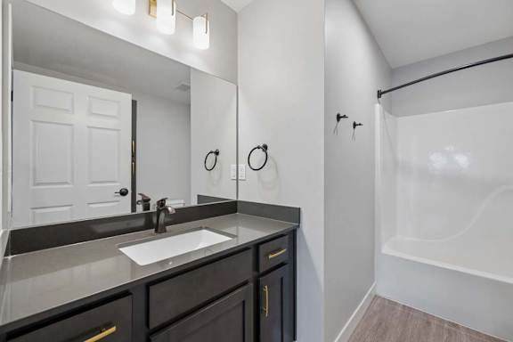 Apartment bathroom with a single-sink vanity, dark cabinetry, a large mirror, and a tub-shower combination with a white surround and modern black fixtures.