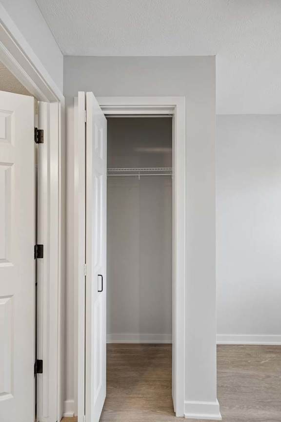 Apartment closet with built-in shelving and a hanging rod, featuring a white bifold door, neutral walls, and wood-style flooring.
