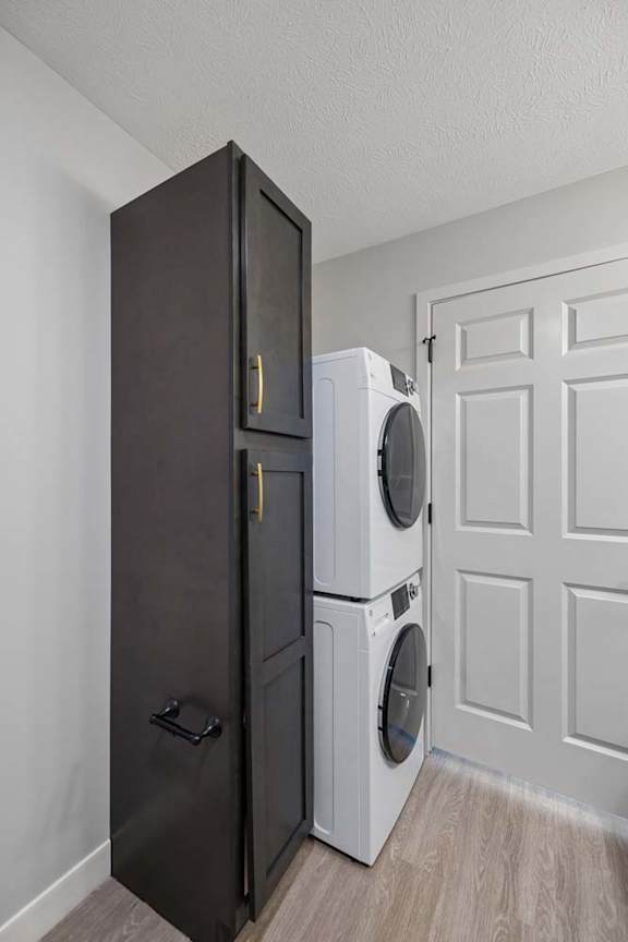 Stacked front-load washer and dryer with a tall dark storage cabinet in an apartment laundry closet featuring light flooring and a white paneled door.