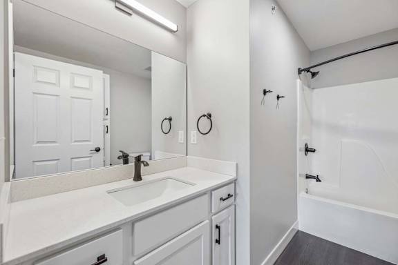 Apartment bathroom with white vanity, black fixtures, and tub-shower combination with surround.