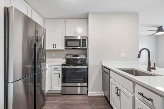 Apartment kitchen with white cabinetry, stainless steel appliances, and oversized peninsula with built-in sink.