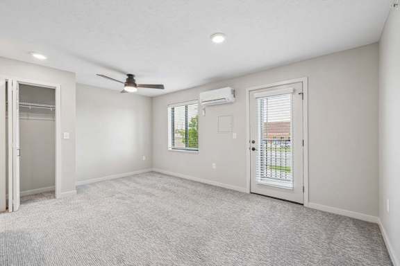 Apartment living area with ceiling fan, large window, and glass door leading to a private balcony.