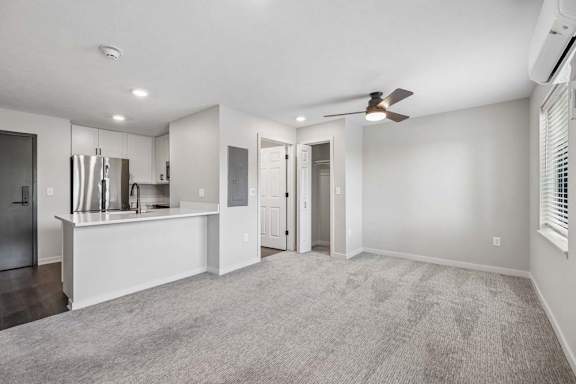 Open apartment living area with neutral carpeting, ceiling fan, and breakfast bar connected to the kitchen.