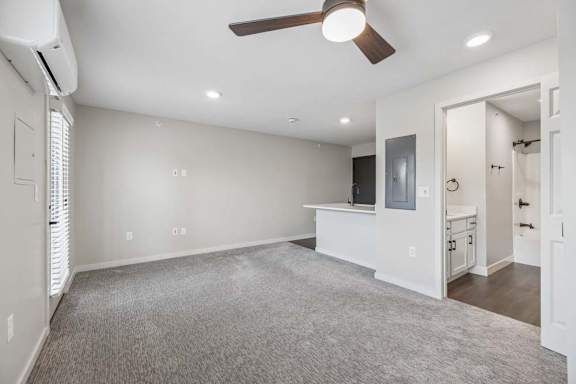 Open apartment living area with ceiling fan, neutral carpeting, and breakfast bar overlooking the kitchen.