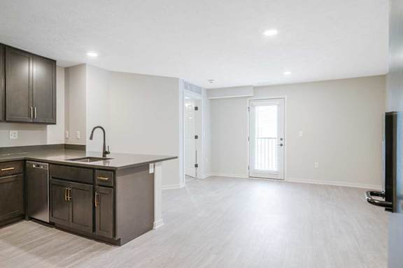 An empty living room and a kitchen with dark cabinets in the Dove at the Knock Apartments in Lincoln, NE