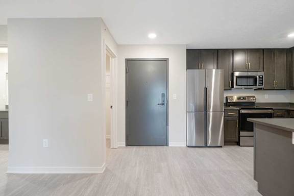 The front door with partial view of the kitchen with dark cabinets and countertops
