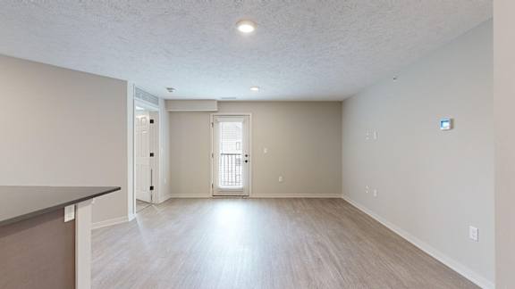 A spacious living room with light wood flooring and white walls.
