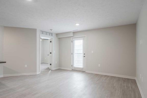 A living room with light vinyl hardwood floors and the doors to the primary bedroom and balcony