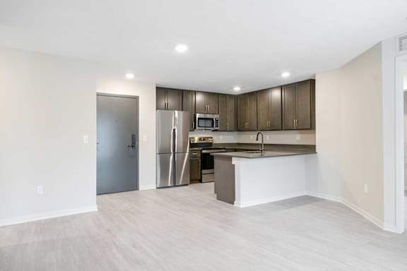 A wide view of the kitchen featuring dark cabinets, stainless steel appliances, and a peninsula countertop