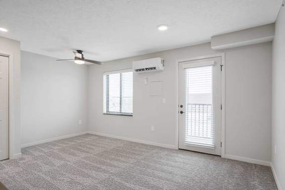 a main room with a ceiling fan, mounted A/C, and a door to the balcony
