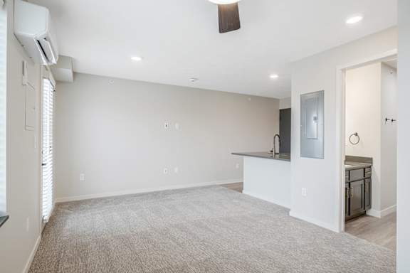 A spacious living room with a carpeted floor and a television on the wall.