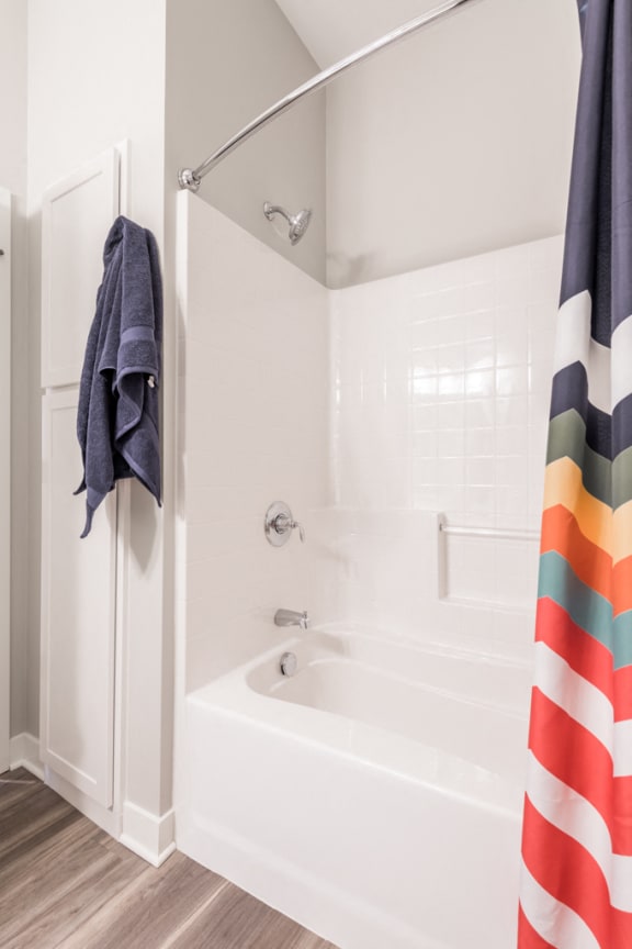 white tub/shower with striped rainbow curtain and a blue towel handing next to it