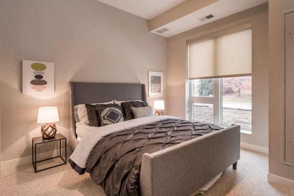 bedroom with large window, queen sized bed, and nightstands with lit lamps
