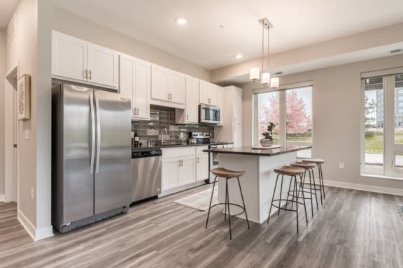 kitchen with white cabinets, dark gray counters and stainless steel appliances. includes island with bar stools
