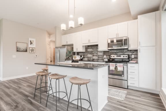 kitchen with white cabinets, dark gray counters and stainless steel appliances. includes island with bar stools