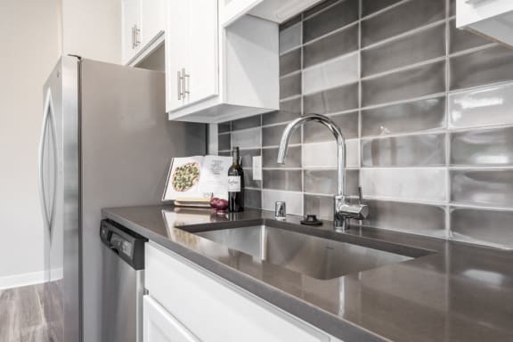 wall of kitchen with dark gray and white backsplash, stainless steel sink and appliances, plus white cabinets