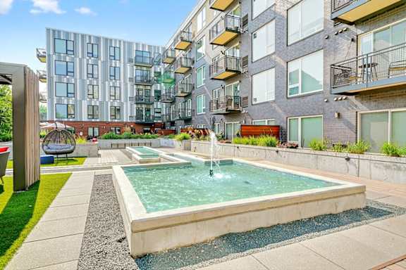 A rectangular concrete water fountain with a central spray feature in a landscaped Zen garden in an apartment courtyard.