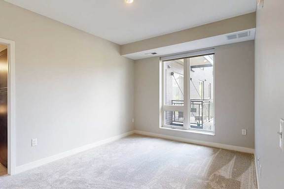 A carpeted bedroom with a floor-to-ceiling window.