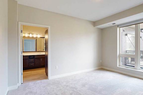 A carpeted bedroom with a floor-to-ceiling window and an attached bathroom.
