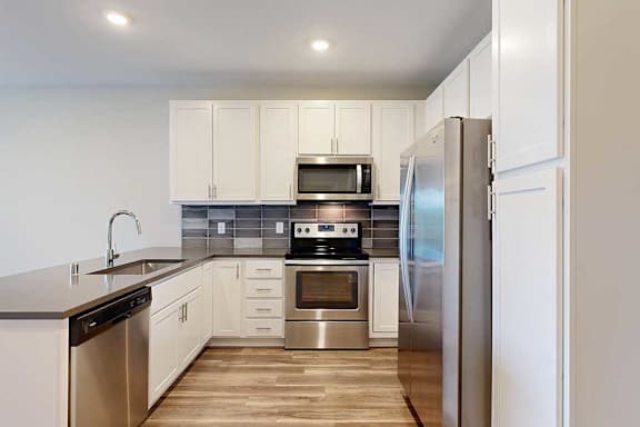 A kitchen with white wooded cabinets, quartz countertops, a peninsula, stainless steel appliances, and a designer backsplash.