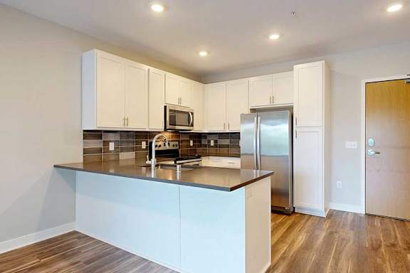 A kitchen with white wooded cabinets, quartz countertops, a peninsula, stainless steel appliances, and a designer backsplash.