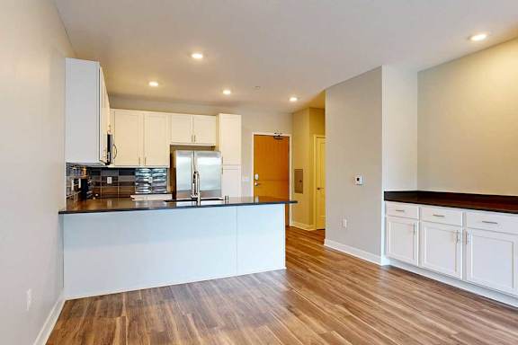 A kitchen with white wooded cabinets, quartz countertops, a peninsula, stainless steel appliances, and a designer backsplash.