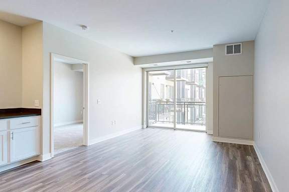 A living room with hardwood-style flooring and a sliding glass door to a balcony.