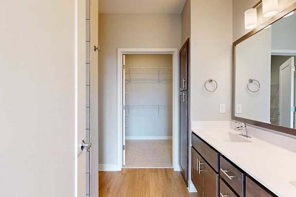 A bathroom with a double sink marble vanity and dark wooden cabinets, connected to a walk-in closet.