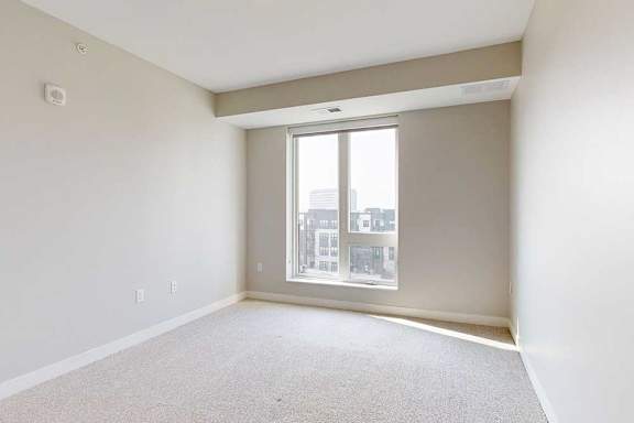 A carpeted bedroom with a floor-to-ceiling window.