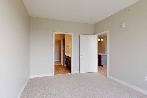A carpeted bedroom with an attached bathroom and a door open to the living room.