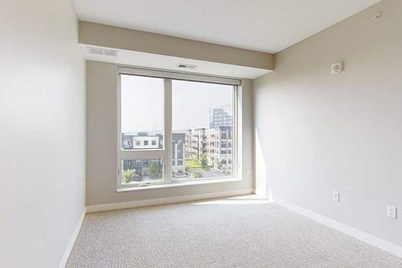 A carpeted bedroom with a floor-to-ceiling window.
