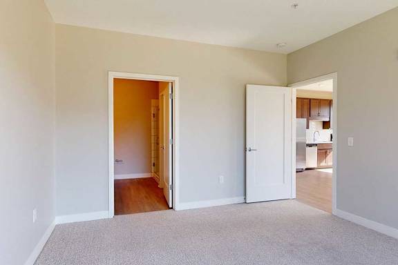A carpeted bedroom with an attached bathroom and a door open to the living room.