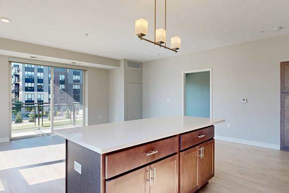 A kitchen with dark wood cabinets and a large island in front of a spacious living room.