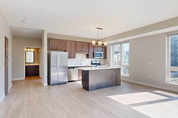 A living room with hardwood-style flooring, connected to a kitchen with dark wood cabinets, a large island, quartz countertops, and stainless steel appliances.