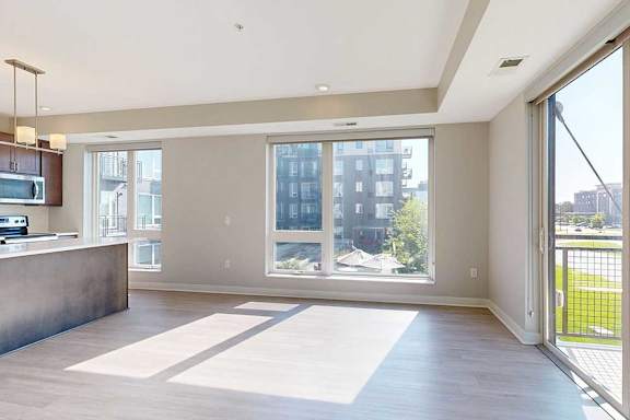 A living room with floor-to-ceiling windows, hardwood-style flooring, and a sliding glass door to a balcony.
