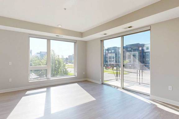 A living room with floor-to-ceiling windows, hardwood-style flooring, and a sliding glass door to a balcony.