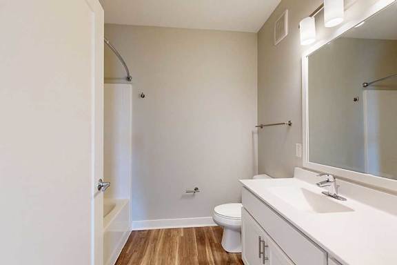 A bathroom with a marble vanity, white wooden cabinets, and a tub shower.