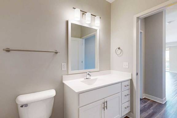 A bathroom with a marble vanity, white wooden cabinets, and a mirror with overhead lighting.