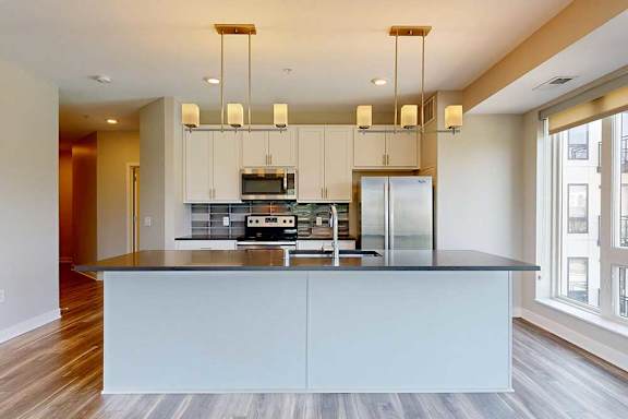 A kitchen with white wooden cabinets, quartz countertops, a large island, stainless steel appliances, and a designer backsplash.