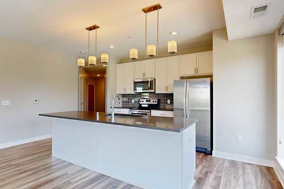 A kitchen with white wooden cabinets, quartz countertops, a large island, stainless steel appliances, and a designer backsplash.
