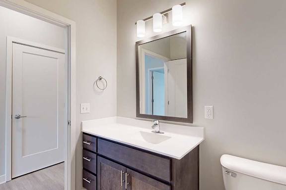 A bathroom with a marble vanity, dark wooden cabinets, and a mirror with overhead lighting.