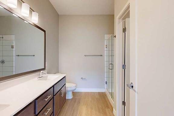 A bathroom with a marble vanity, dark wooden cabinets, and a walk-in shower.