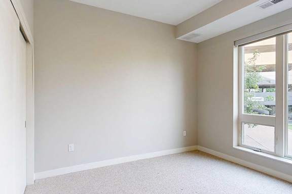 A carpeted bedroom with a floor-to-ceiling window.