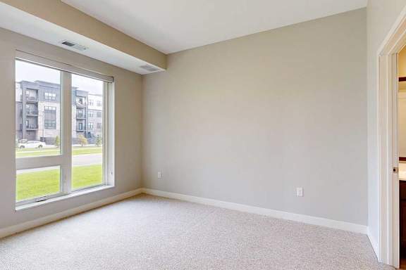 A carpeted bedroom with a floor-to-ceiling window.