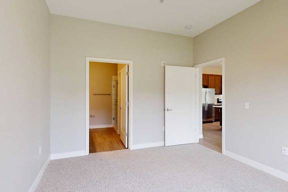 A carpeted bedroom with an attached bathroom and a door open to the living room.